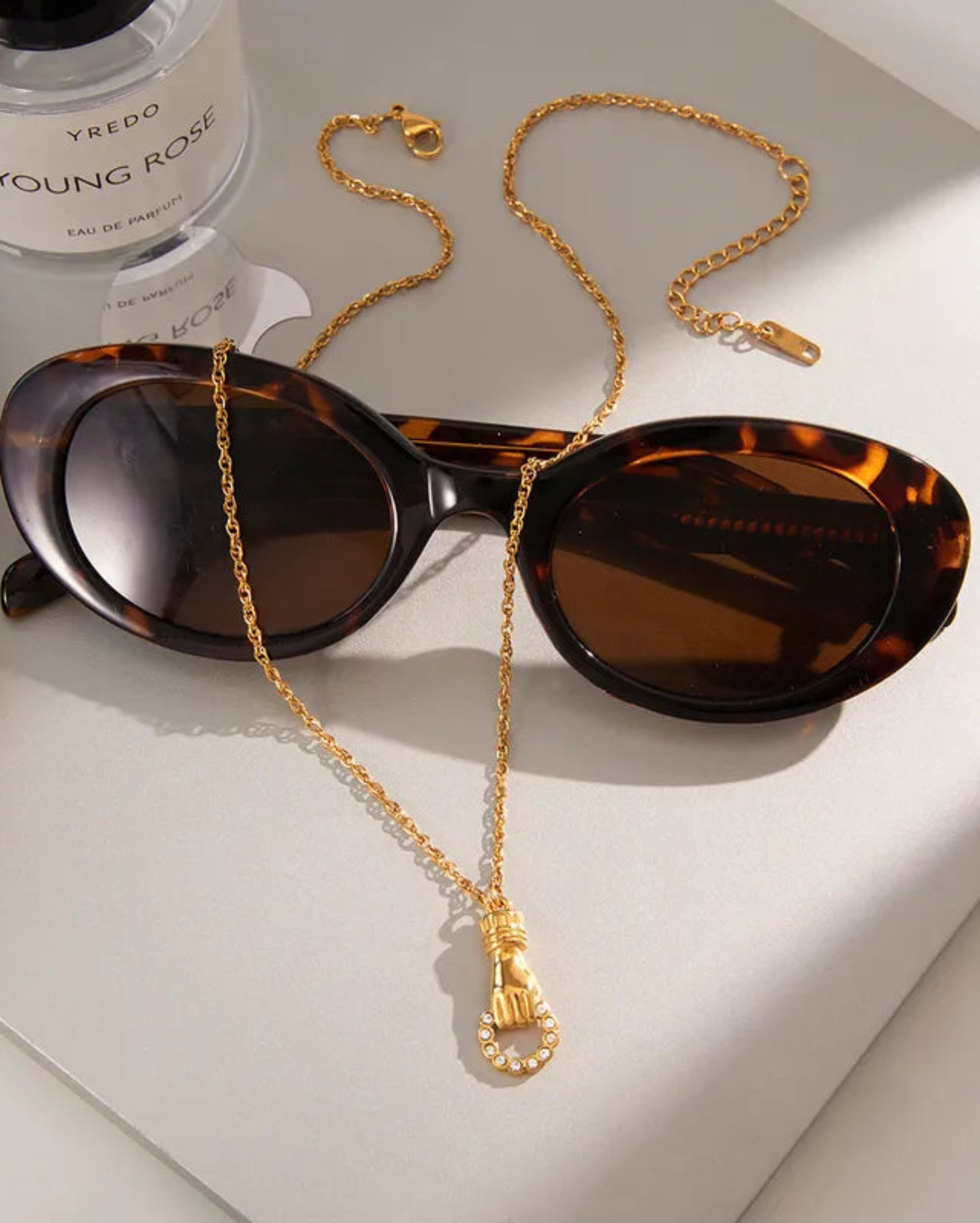 Black cat-eye sunglasses with a gold chain necklace strap featuring a small gold pendant, displayed on a clean white background.