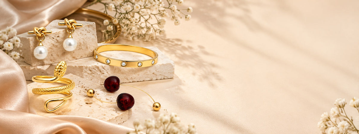 Pabeena pearl drop knot earrings, a crystal-set gold bangle, a gold snake ring and a red cherry bracelet on cream stone with champagne satin